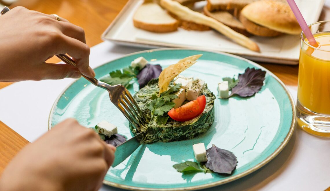 person holding fork and knife slicing vegetable on white ceramic plate